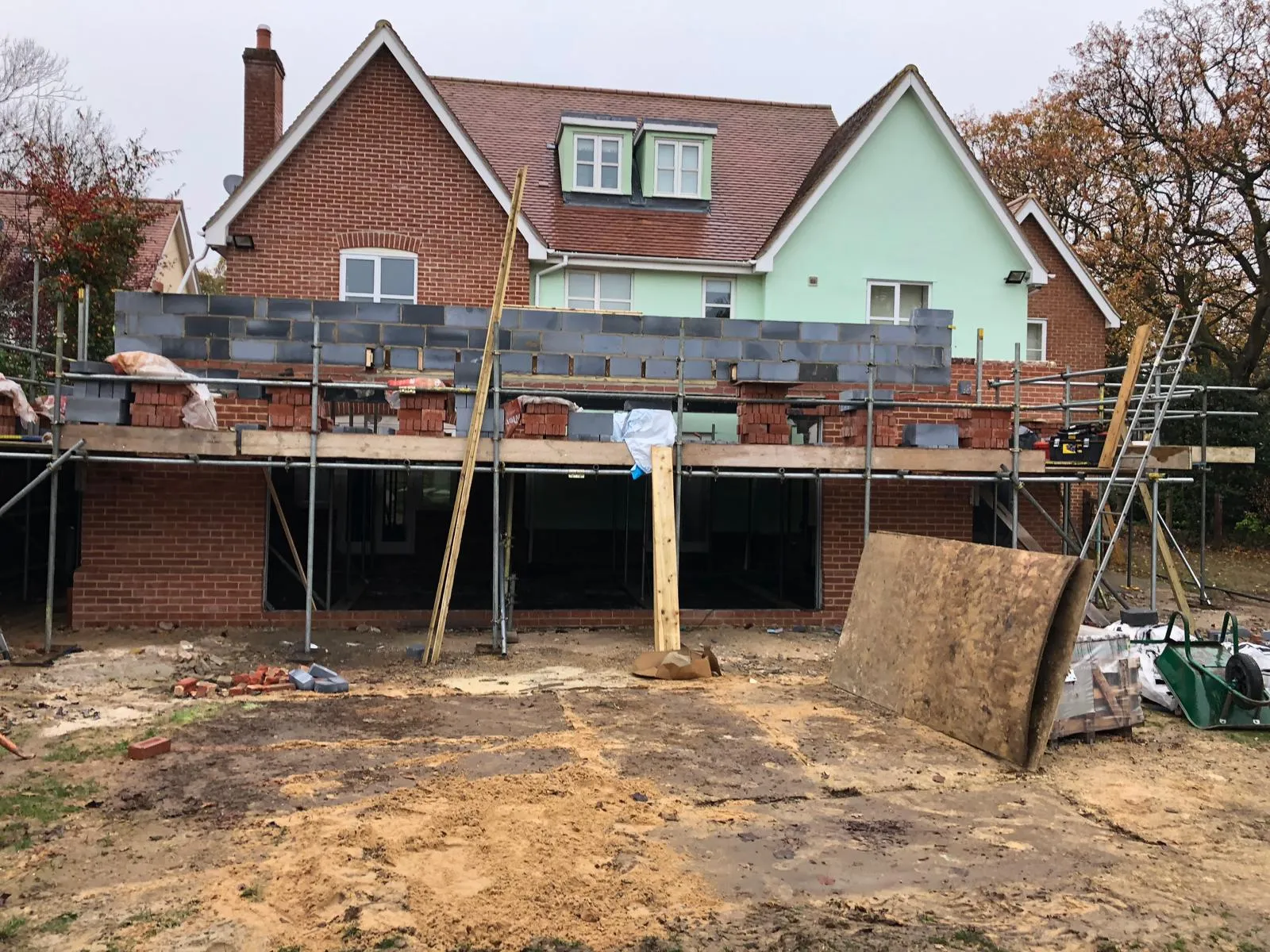 A house extension under construction with scaffolding and new brick walls being built on the ground floor.