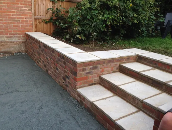 Newly built brick garden wall and natural stone steps with prepared sub-base for a new path or driveway, showcasing hard landscaping expertise.