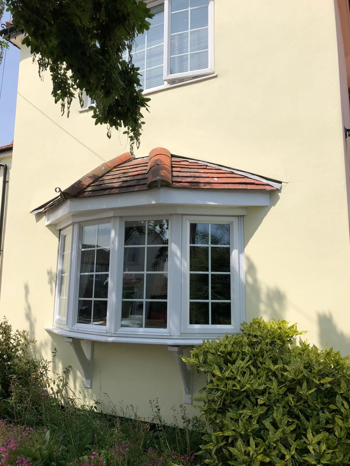 Exterior view of a house with light yellow render and a white uPVC bay window installation.