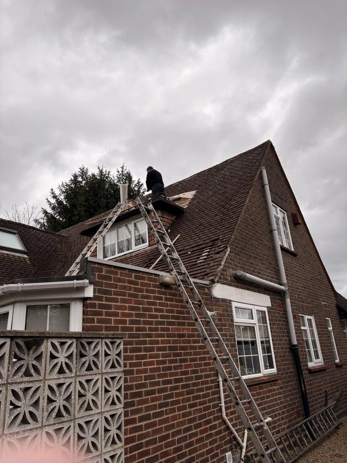 Roofer repairing clay roof tiles and underlay around a dormer window in Slough