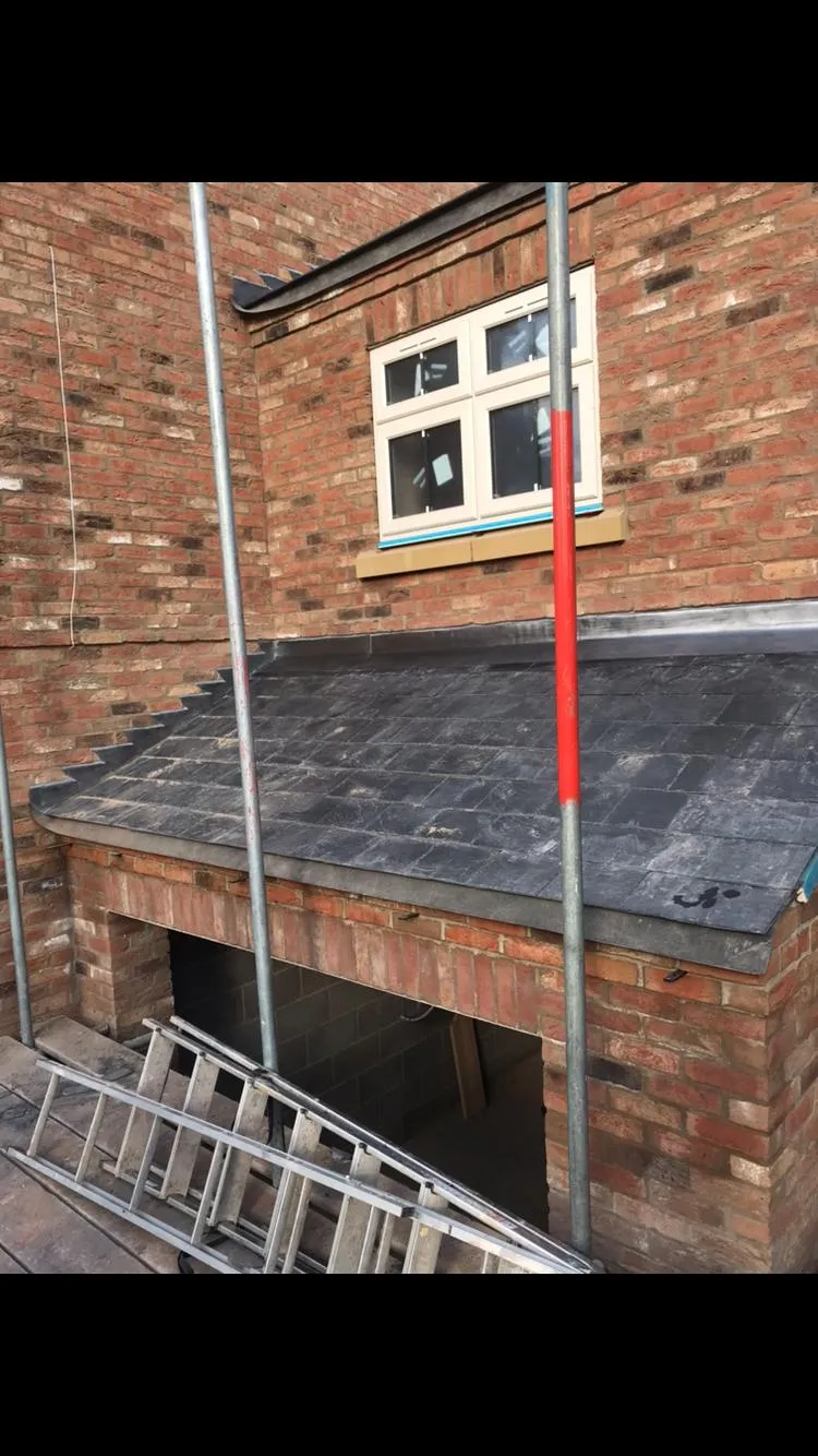 New pitched roof installation with dark tiles on a brick extension or lower building section, showing scaffolding.