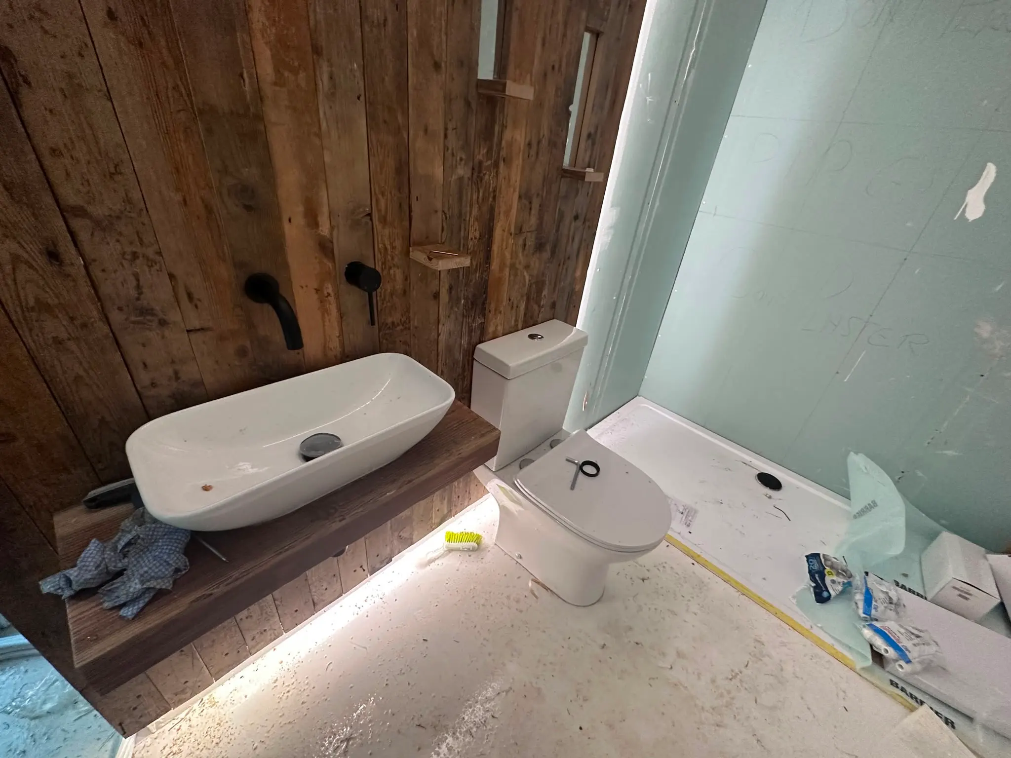 A modern bathroom refurbishment in progress showing a new vessel sink, toilet, and shower tray installation