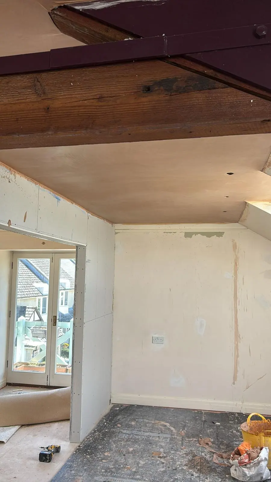A room undergoing premium renovation showing exposed heritage wooden beams, newly plastered ceilings, and unfinished stud walls.