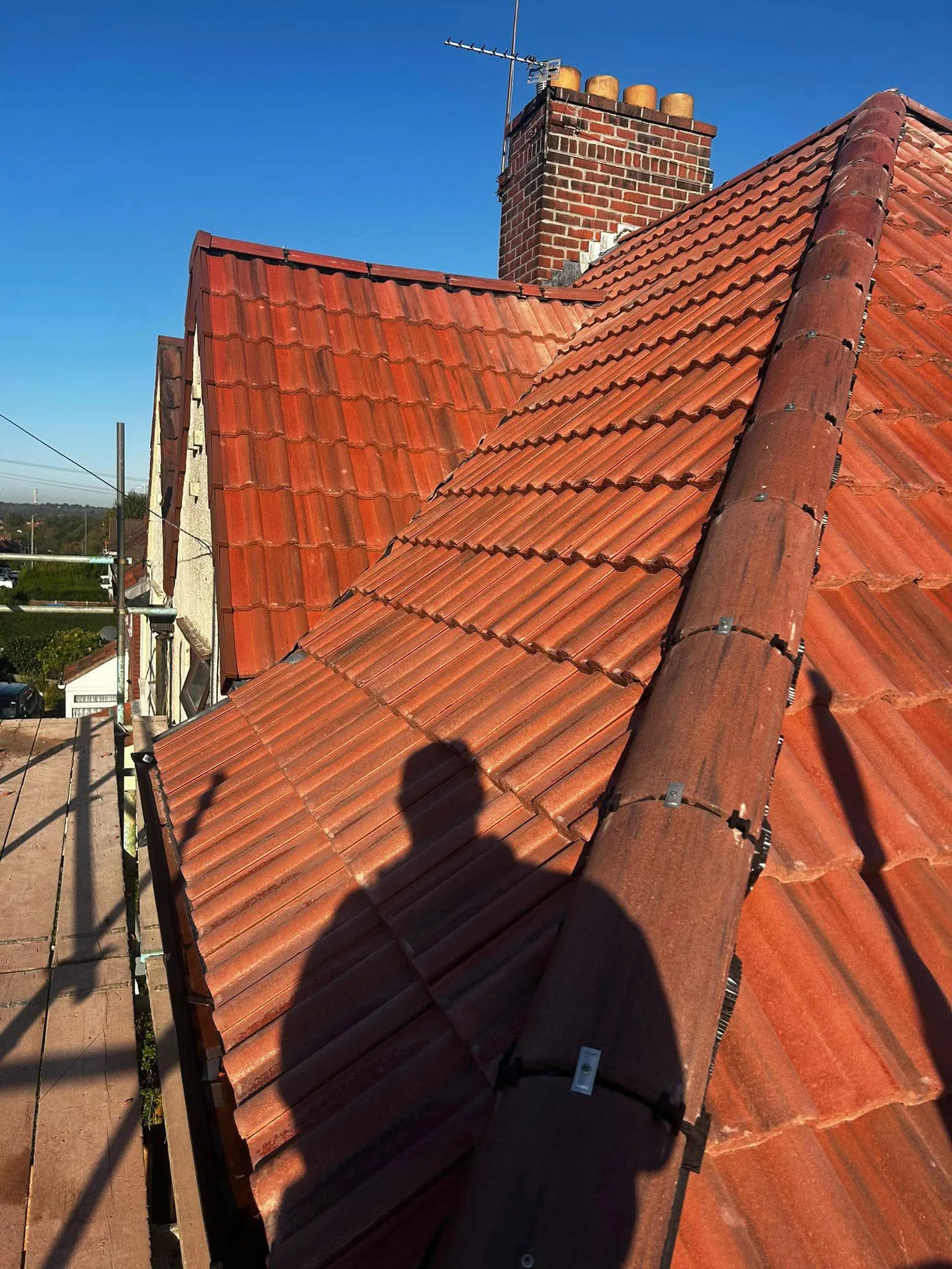 A close-up of red terracotta roof tiles and a brick chimney on a residential house during a roofing project.