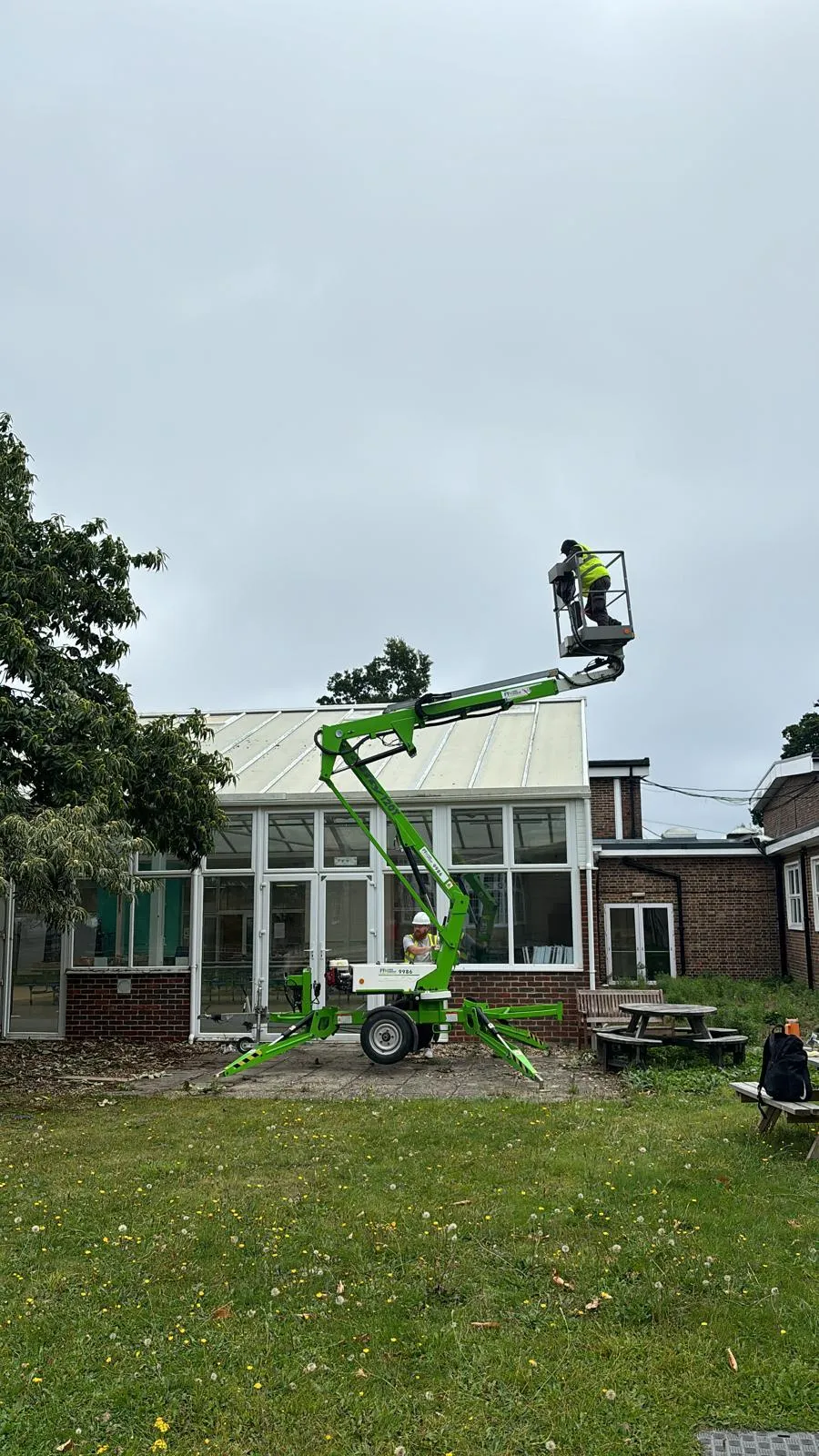 A roofer operating from a green cherry picker on the roof of a conservatory-style building.