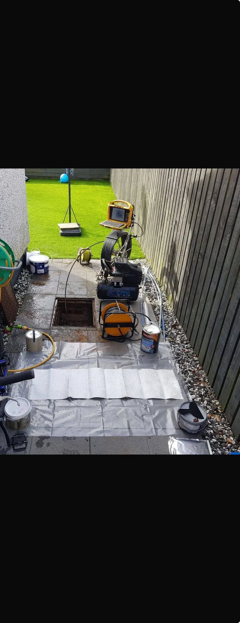 Drainage equipment for CCTV survey and no-dig repairs laid out next to an open manhole in a garden.