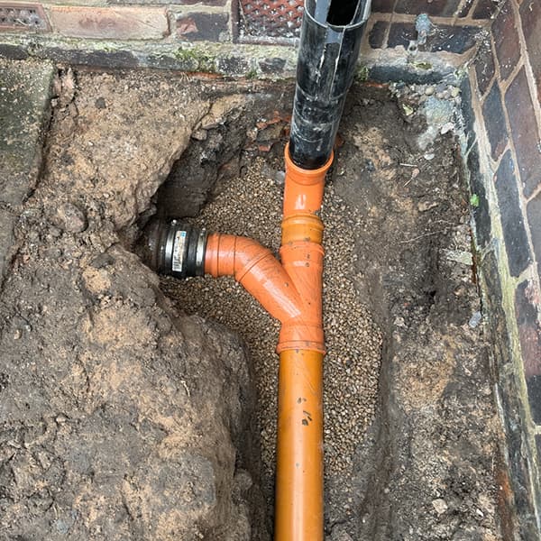Newly installed orange PVC drainage pipes connected in an excavated trench next to a brick building