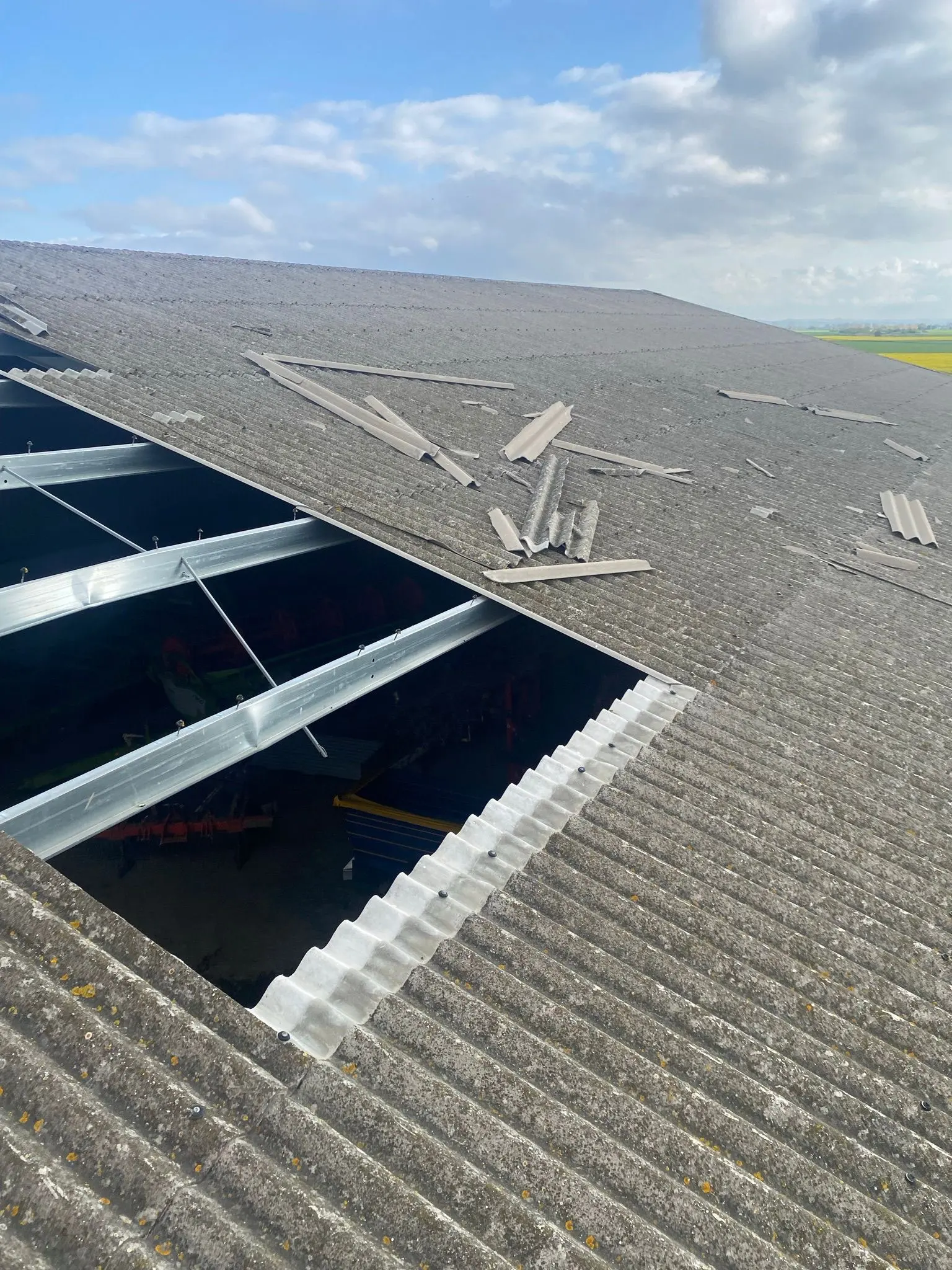 Storm-damaged corrugated roof on an agricultural barn with exposed steel framework and broken panels