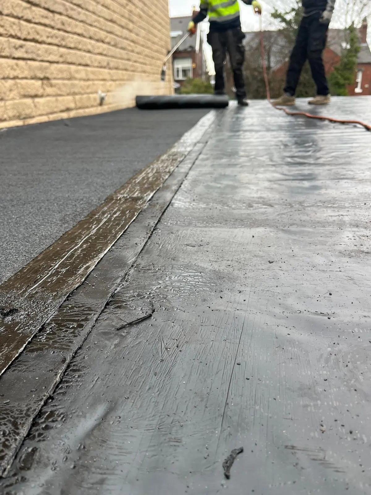 Roofers installing a black torch-on flat roofing membrane on a flat roof