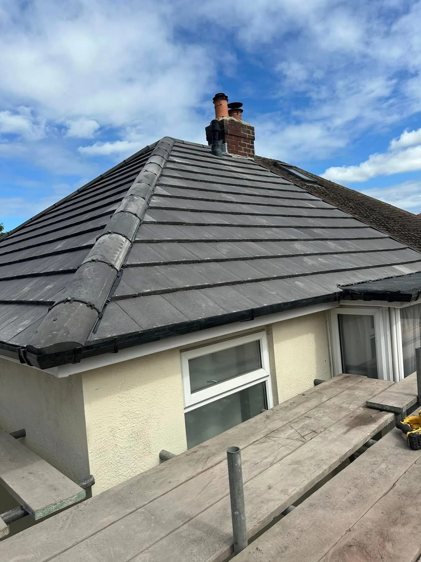 Expertly installed grey tile roofing on a house in Otley, Leeds, showing ridge tiles and chimney repairs with scaffolding.