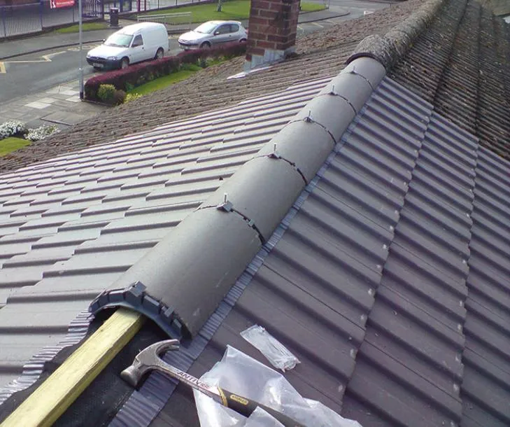 Roofers installing a new dry ridge system on a pitched tiled roof, showing the difference between old mossy ridge and new grey tiles.
