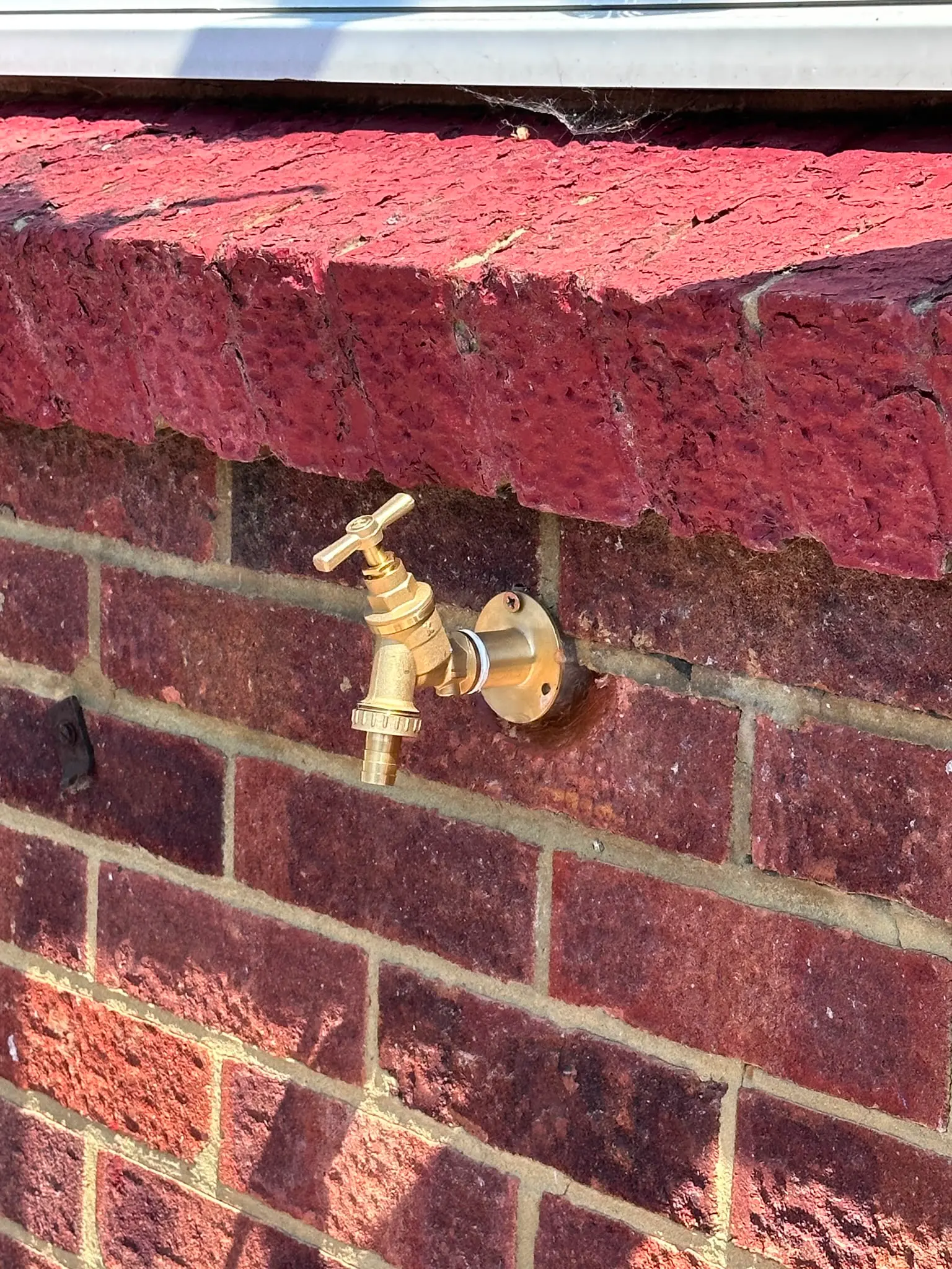 A professionally installed brass outside garden tap on a red brick wall