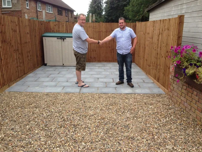 Client and contractor shaking hands on a newly installed patio and gravel garden with new fencing, signifying a completed landscaping project by Elite Paving and Roofing LTD.
