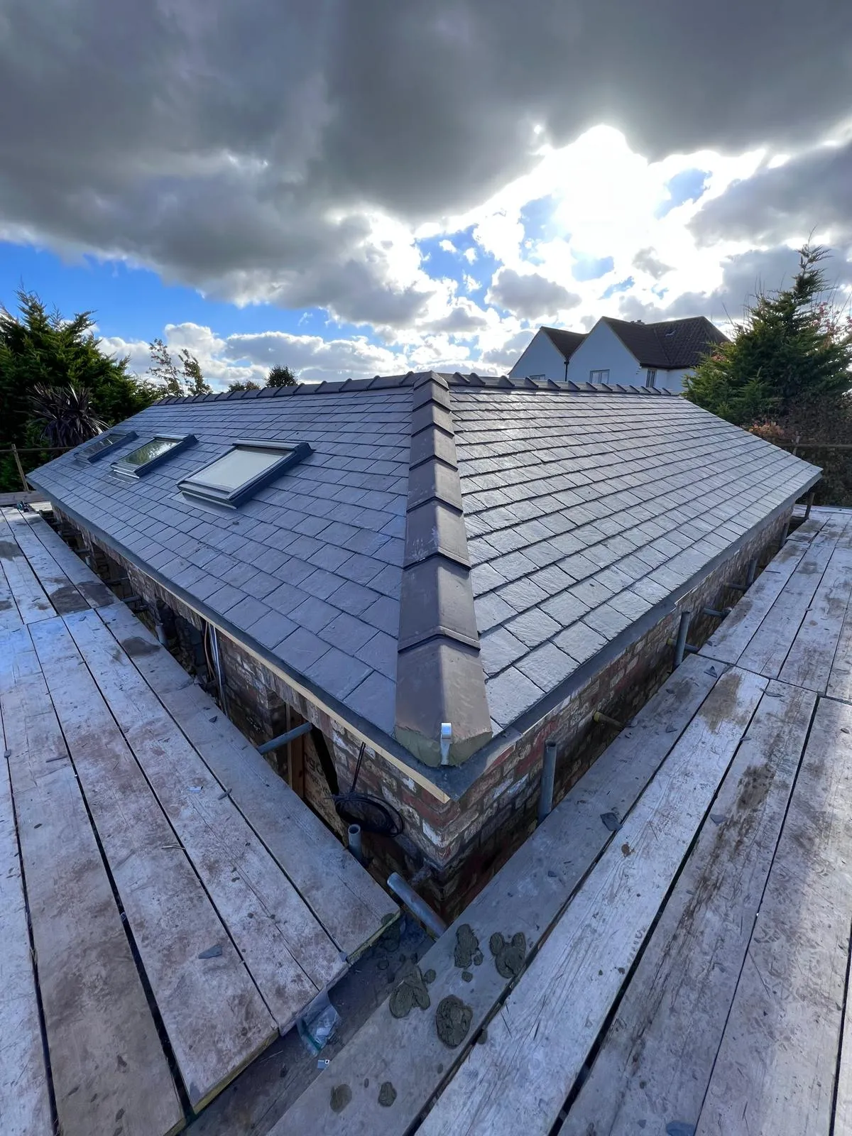 Newly installed dark grey tiled pitched roof featuring several roof windows, with scaffolding visible during the construction process.