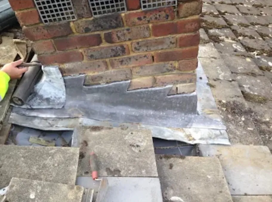 Roofer dressing and installing stepped lead flashing around a brick chimney stack