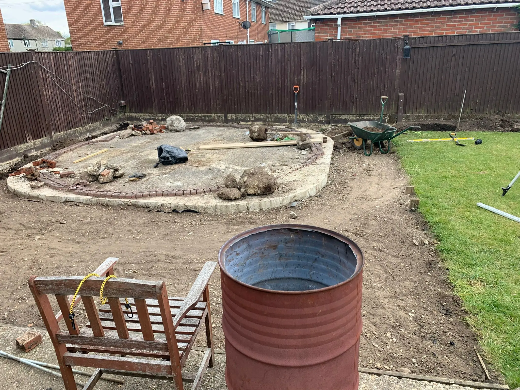 A garden construction site showing groundworks, broken concrete, and tools, representing site clearance and landscaping preparation.