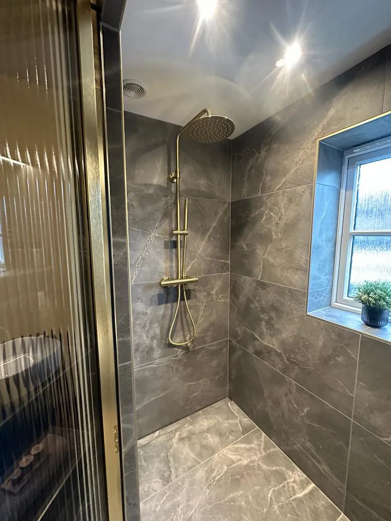 Bespoke luxury walk-in shower installation in Plymouth featuring marble-effect tiling and brushed gold brassware by Sands & Vossen.