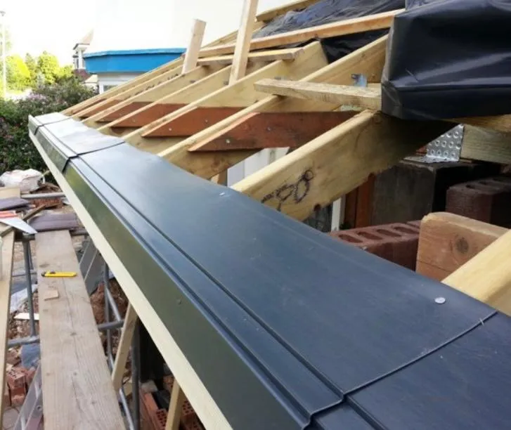 A close-up view of new dark grey UPVC fascia boards being installed on a roof, with the timber rafters and roof underlay visible behind.