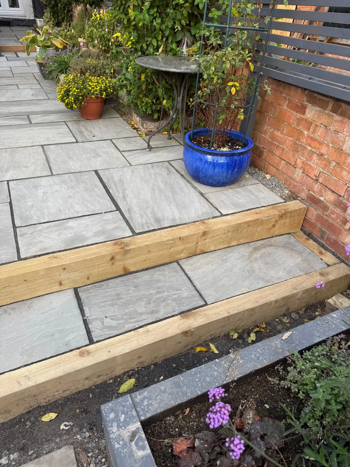 Modern grey paved patio with timber sleeper steps and garden planting.