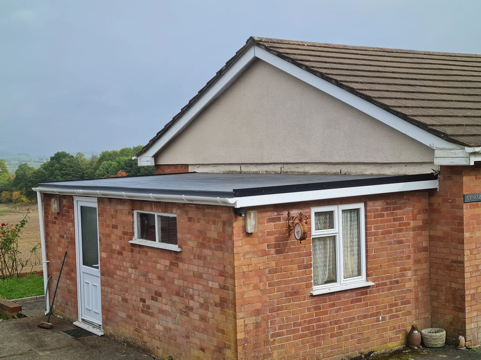 A professional installation of a new black flat roof with white UPVC fascias, soffits, and guttering on a brick extension of a home.
