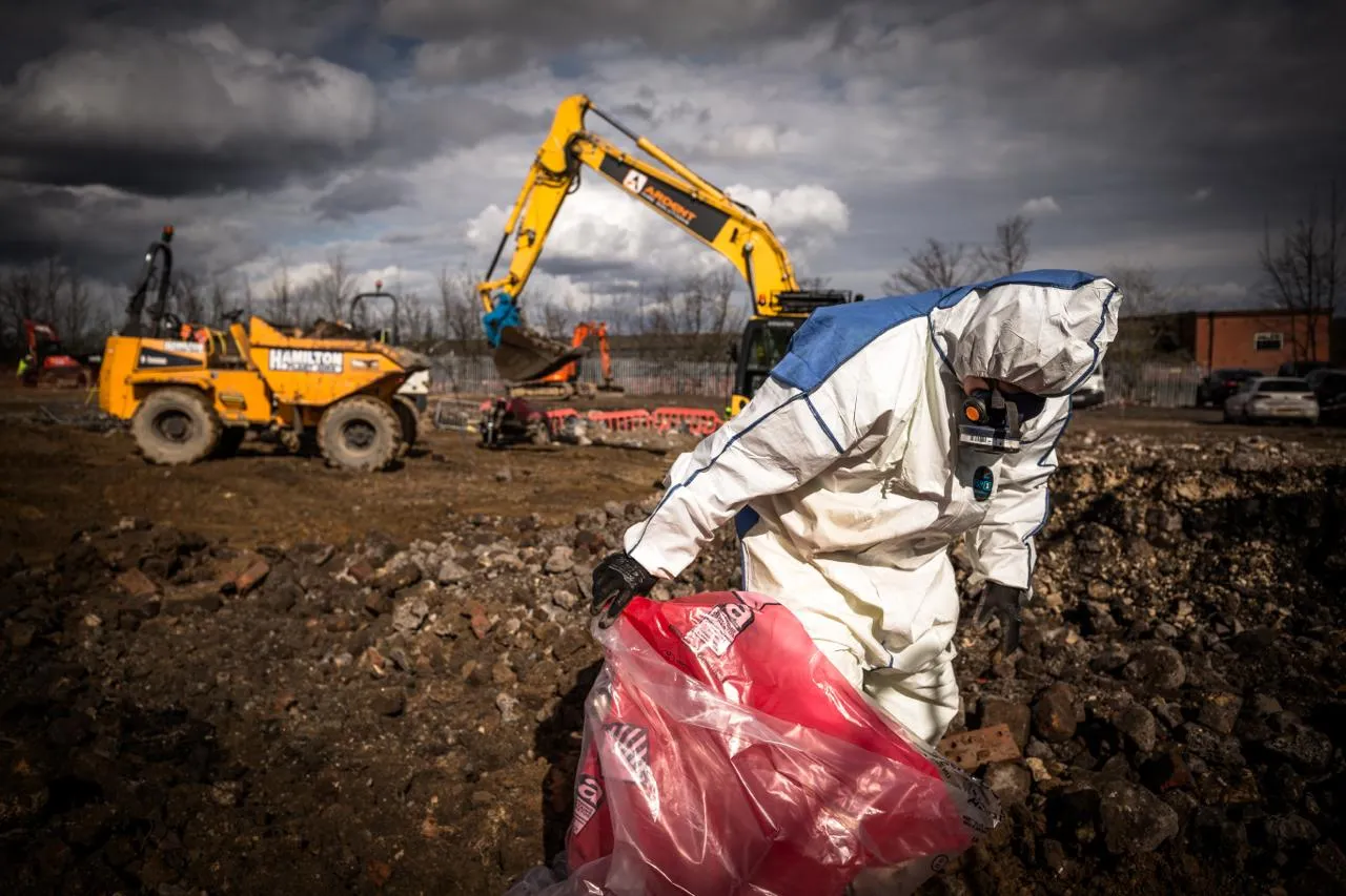 Asbestos removal expert in a hazmat suit on a commercial site, managing hazardous waste with heavy machinery in the background.