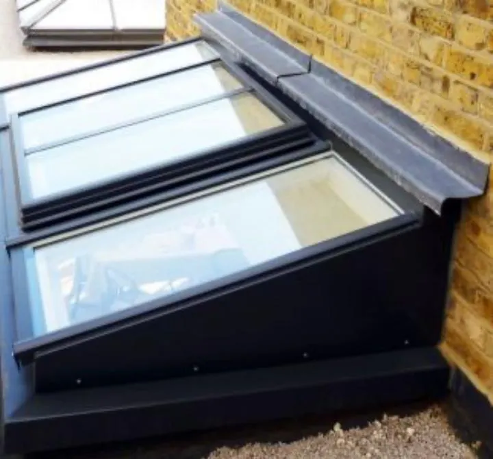 Newly installed Velux windows or rooflights with dark frames and integrated lead flashing on a roof next to a brick wall.