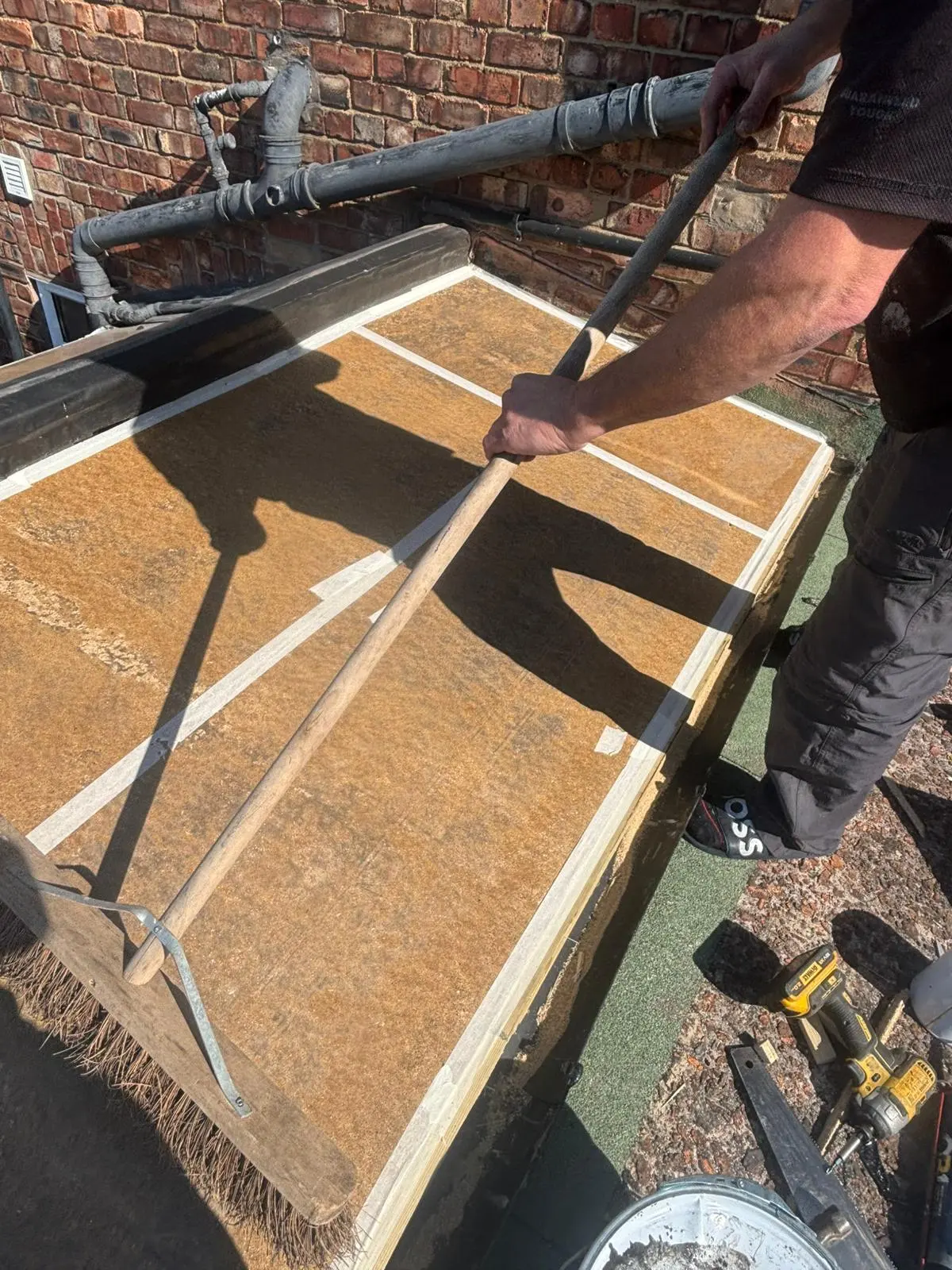 A roofer sweeping a prepared timber deck during a flat roof installation