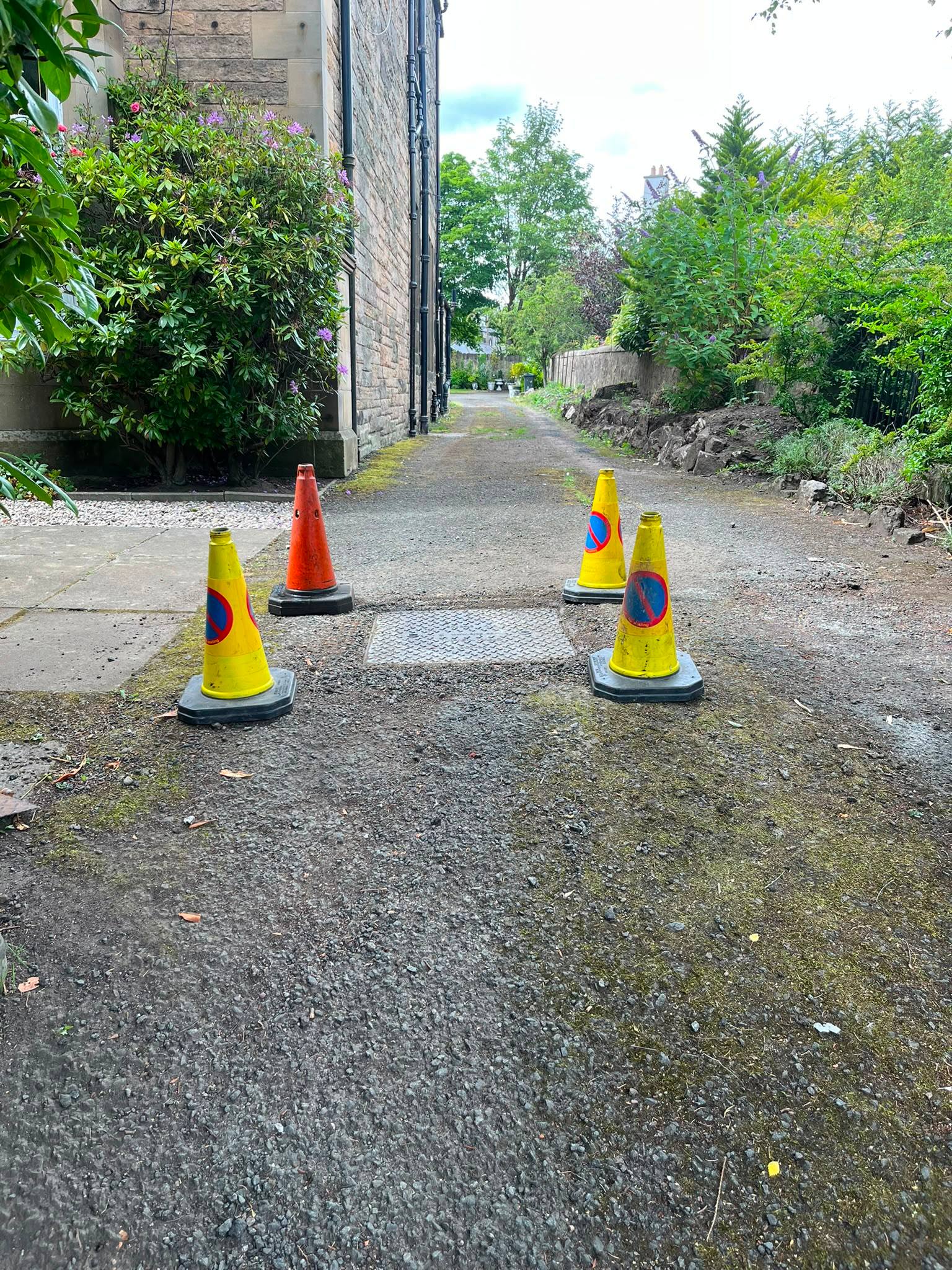 Safety cones surrounding a metal manhole cover on a residential driveway during drainage inspection works