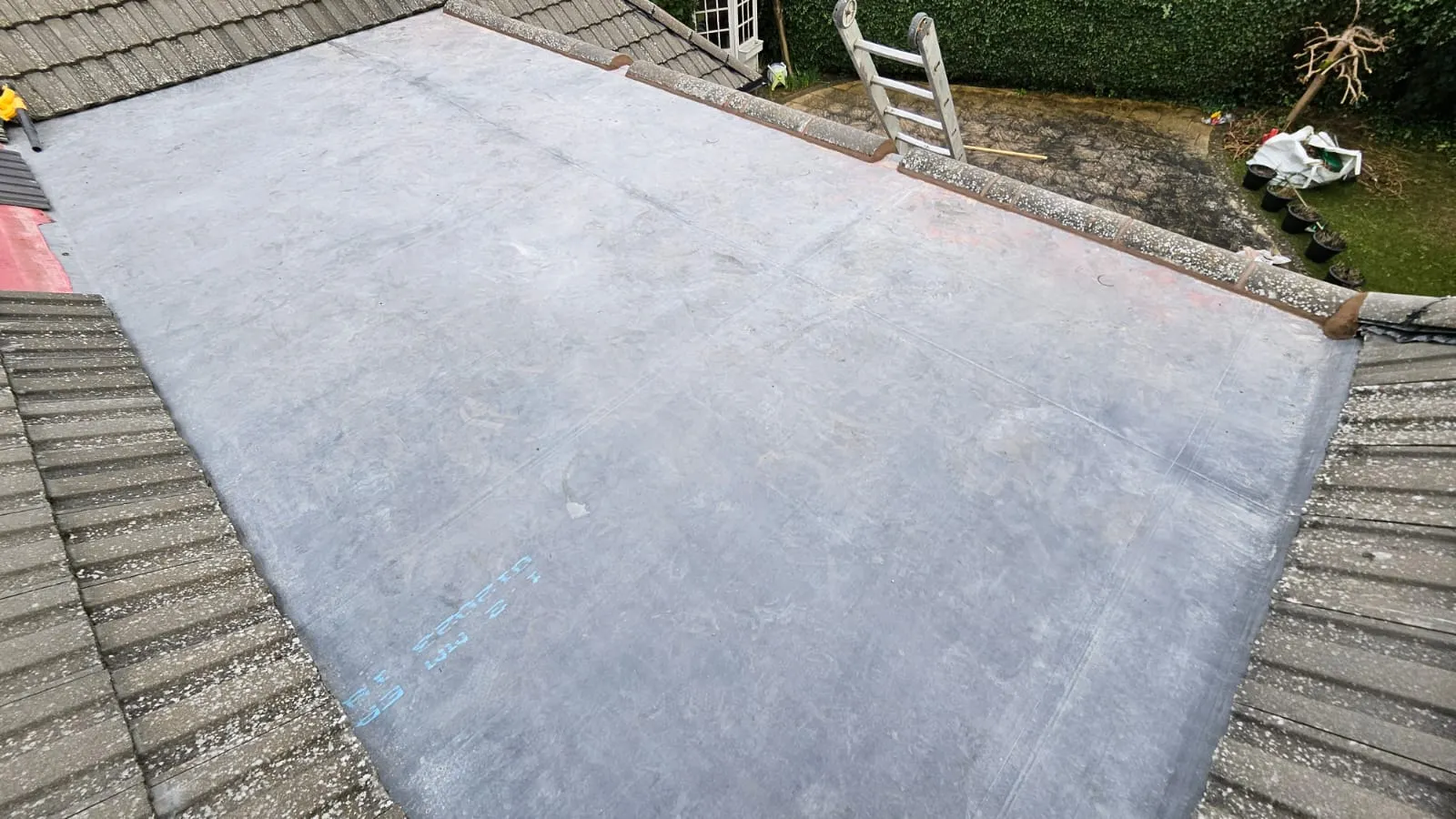 A new dark grey EPDM flat roof installation, showing its seamless surface, next to a tiled pitched roof.