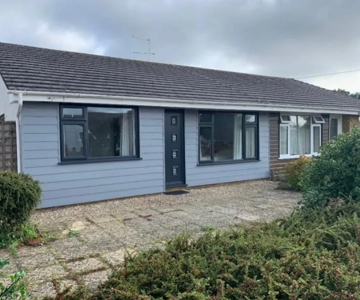Front view of a bungalow with newly installed grey cladding, dark windows, and clean white fascias, soffits, and gutters.