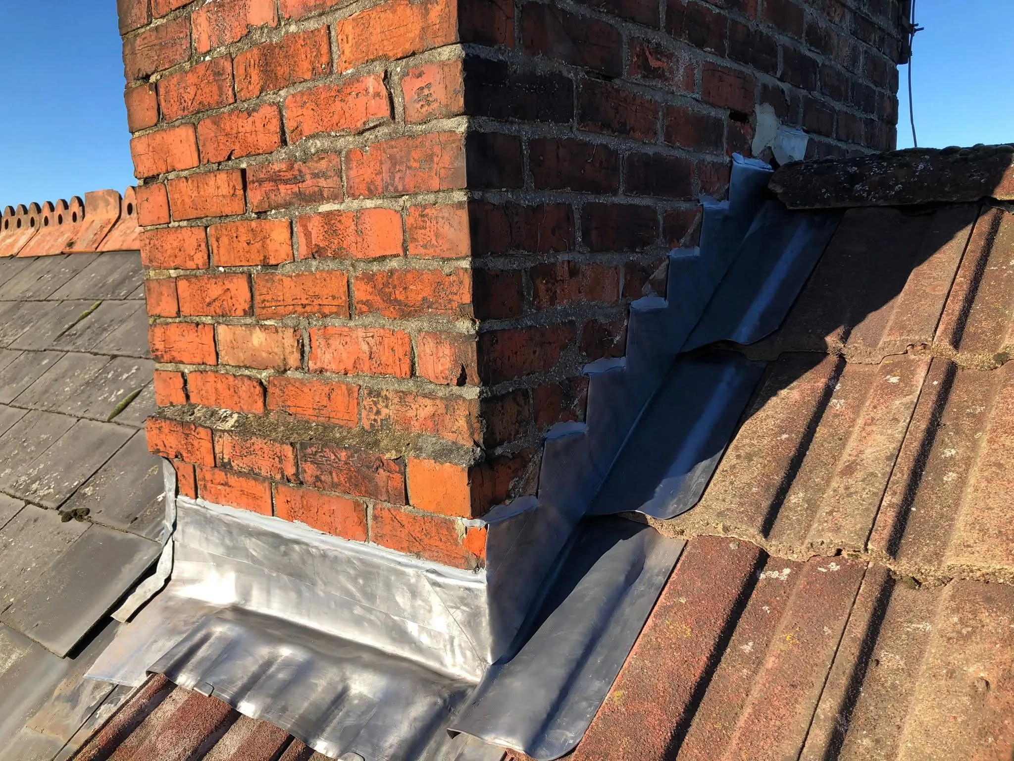 Newly installed lead flashing around the base of a brick chimney on a residential roof.