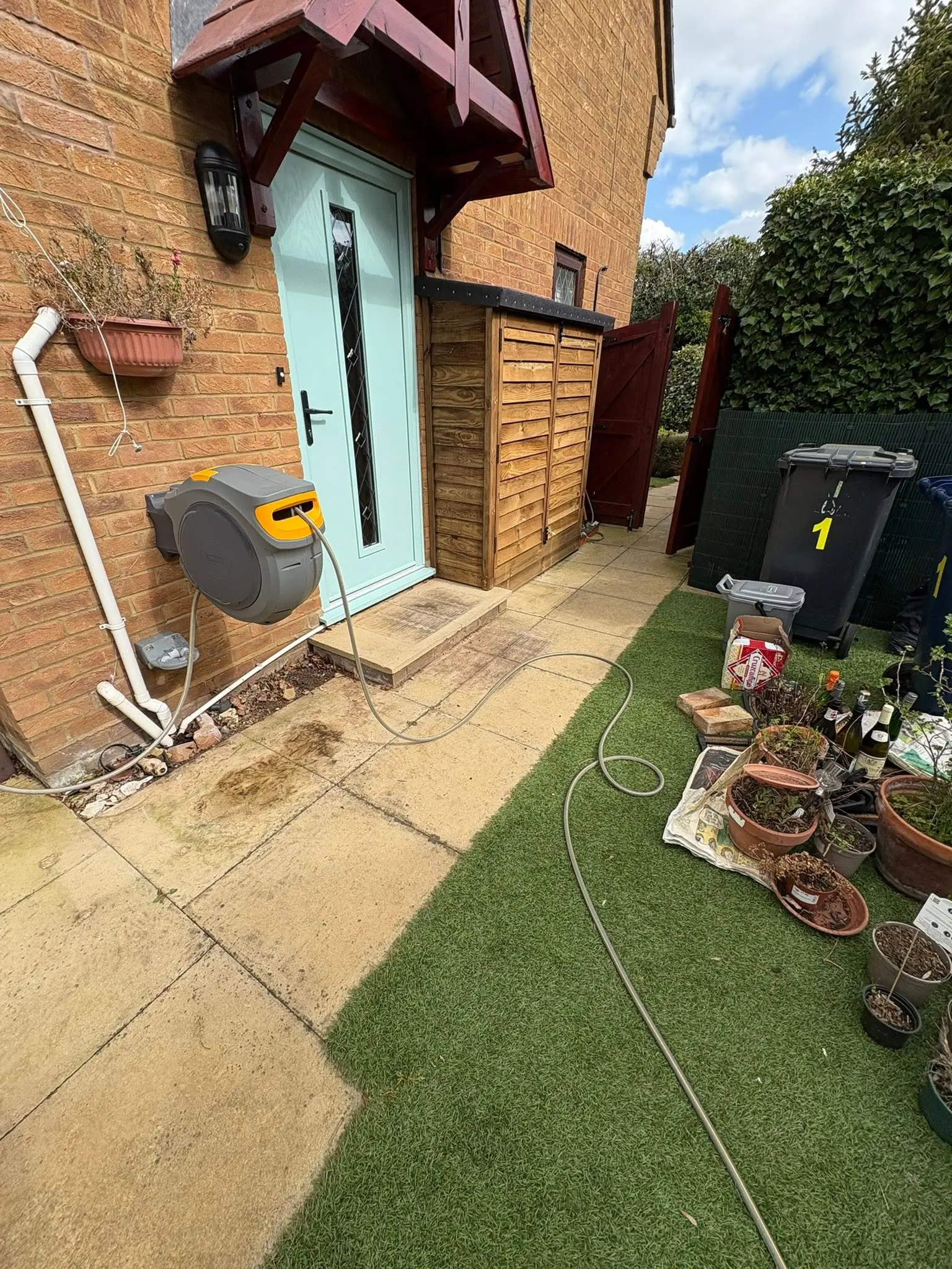 A domestic garden area with a patio, artificial grass, and a hose pipe