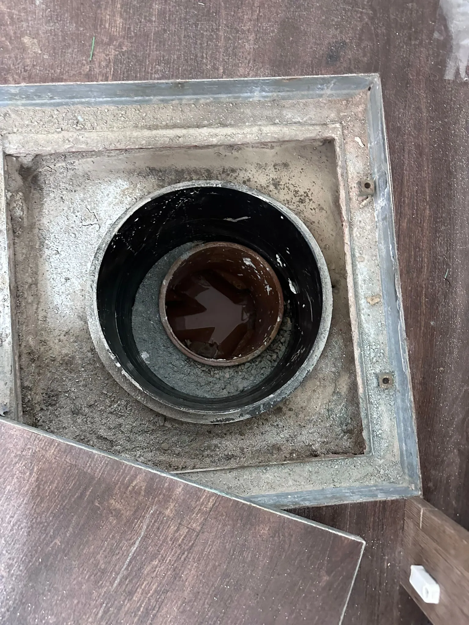 An open internal drainage access point under a floor showing standing water in a clay pipe, requiring inspection.