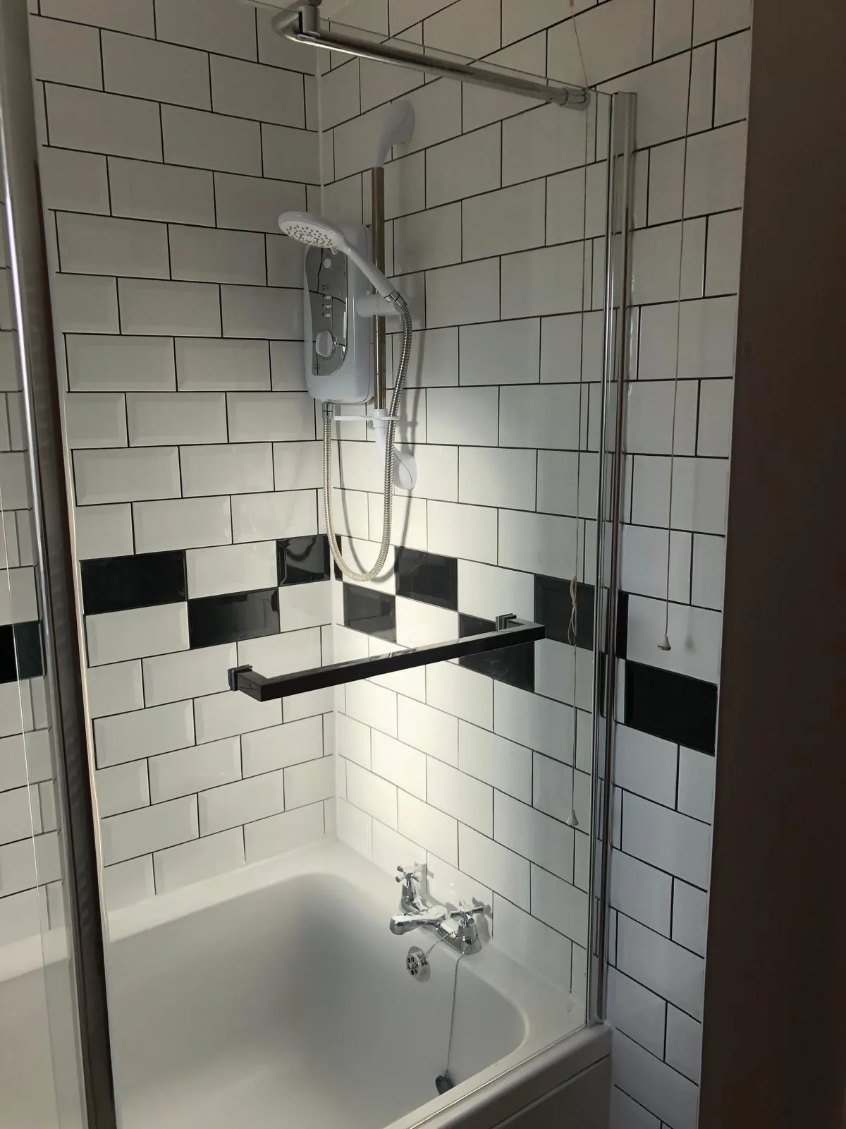 Modern bathroom renovation with a bath, electric shower, white subway tiles, and a glass shower screen.