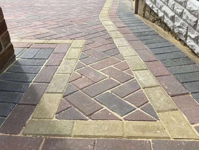 A close-up of a new multi-coloured block paved driveway with intricate herringbone patterns and a contrasting border, showcasing quality craftsmanship.