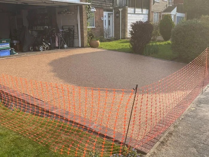 A new resin-bound driveway with brick border and orange safety fencing in front of a house.
