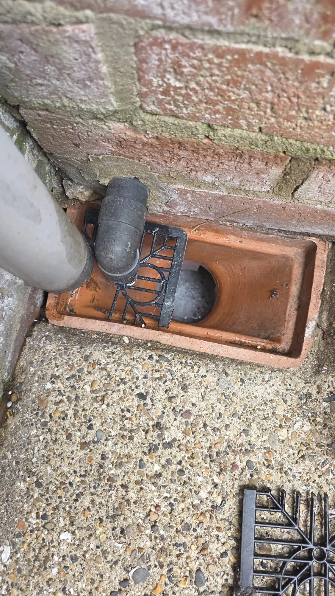 A close-up of a damaged outdoor drain with water pooling inside.