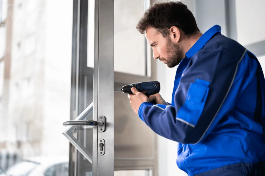 A professional locksmith in a blue uniform installing or repairing a modern door lock with a drill, demonstrating lock change and upgrade services.