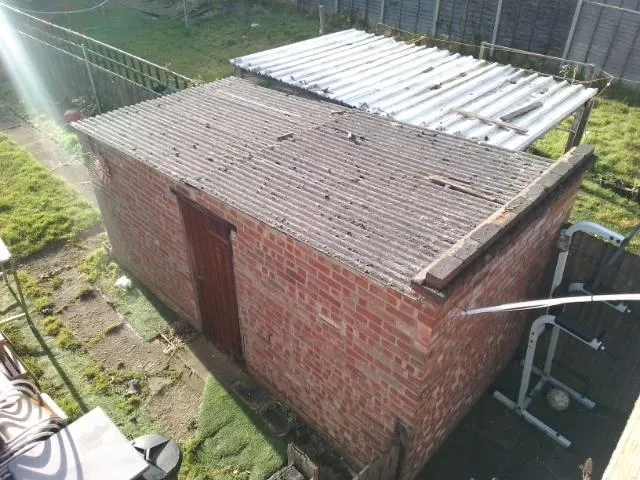 A brick shed with a corrugated roof in a garden, indicative of asbestos garage roof removal services.