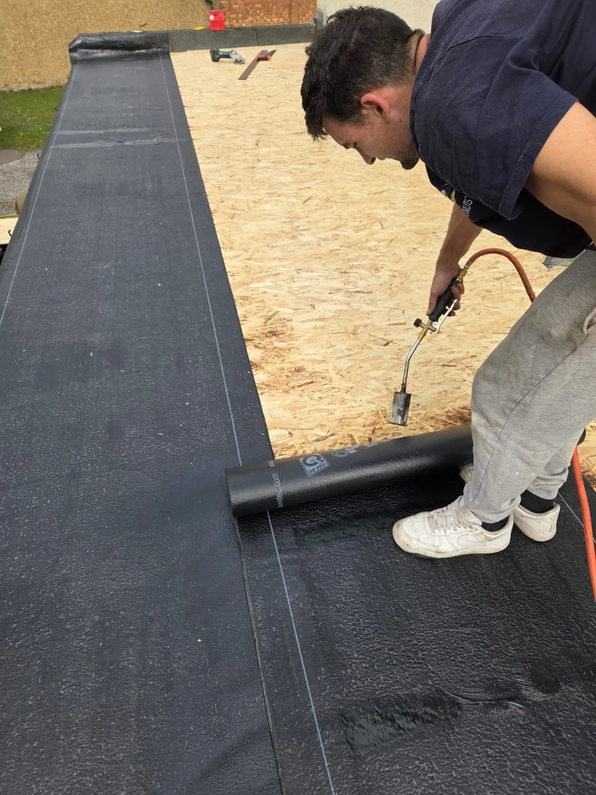 A roofer applying torch-on felt to a new flat roof installation in Cornwall