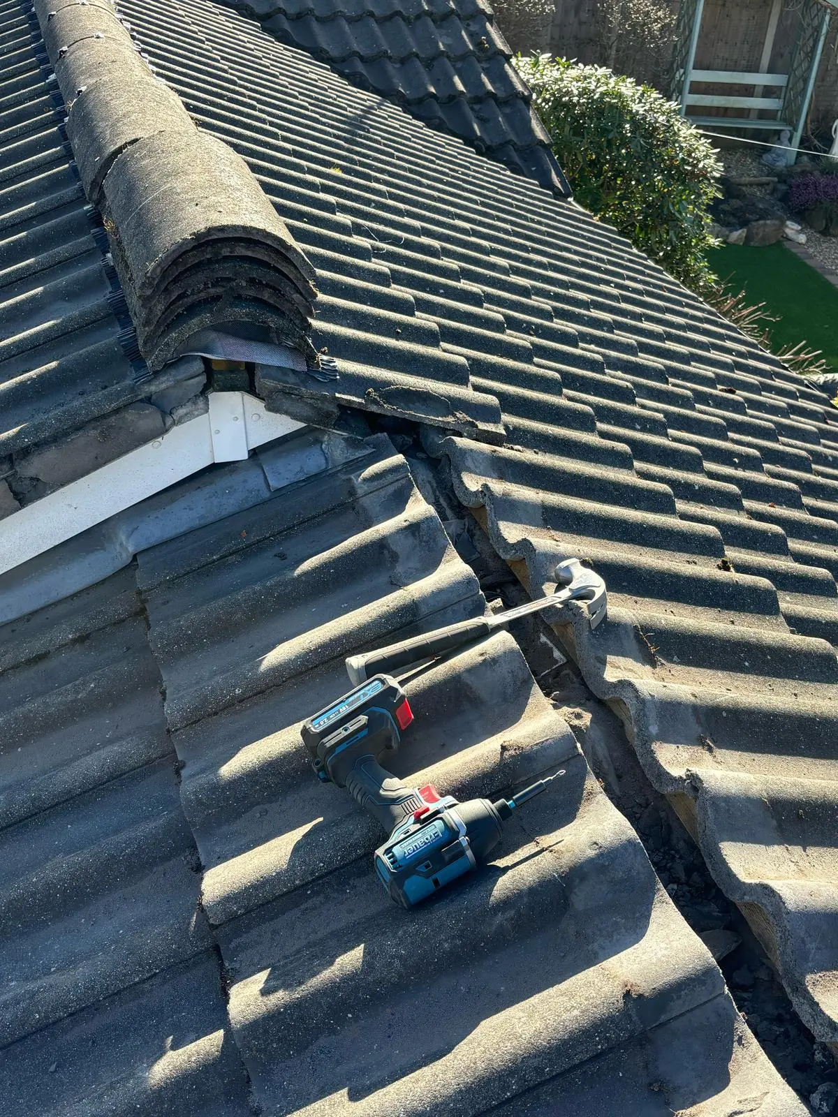 Tiled roof repair in progress showing a hammer and drill resting on concrete roof tiles