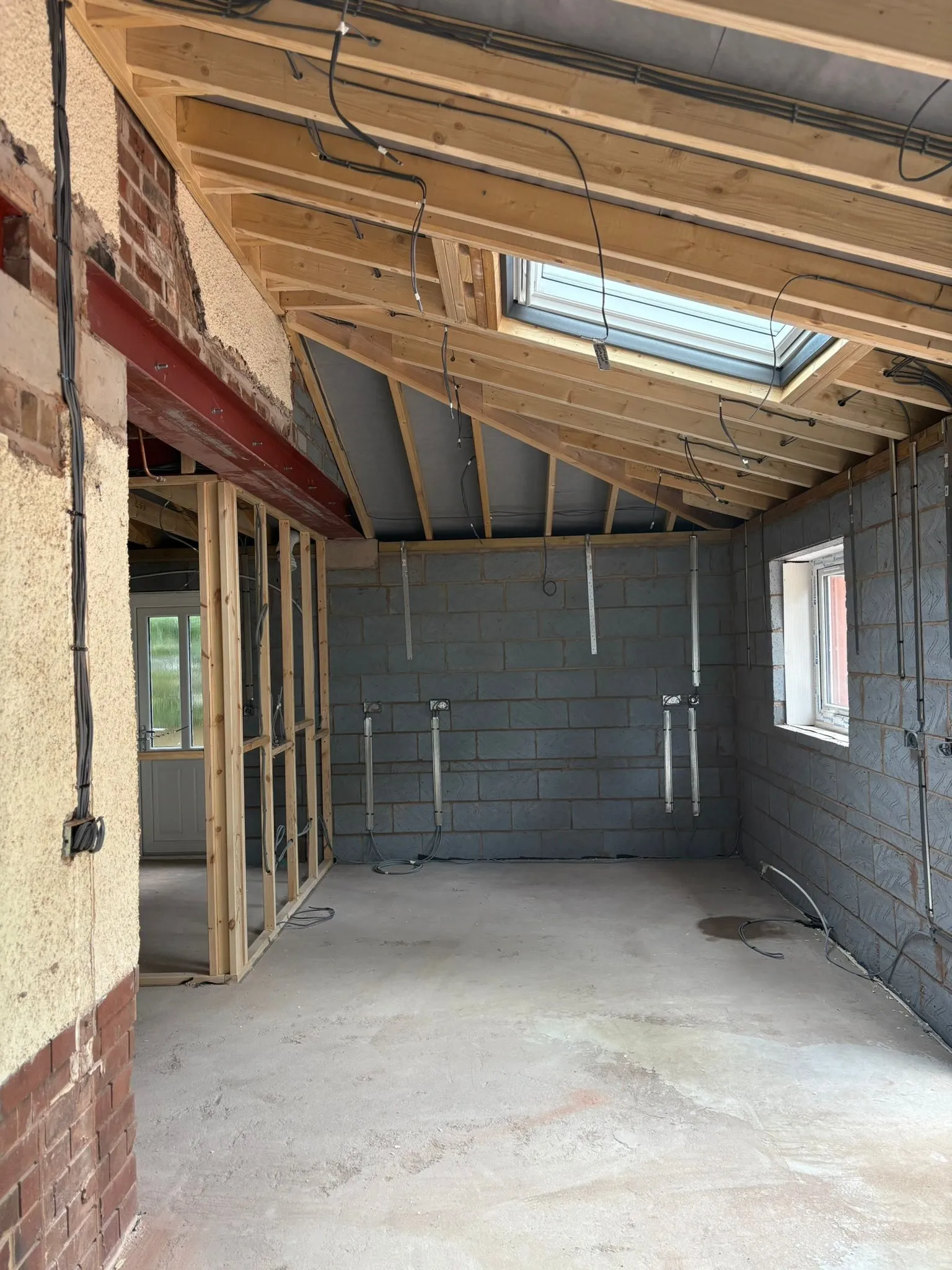 Interior of a single-storey home extension during construction, showing the roof structure with a skylight, new walls, and electrical cabling.