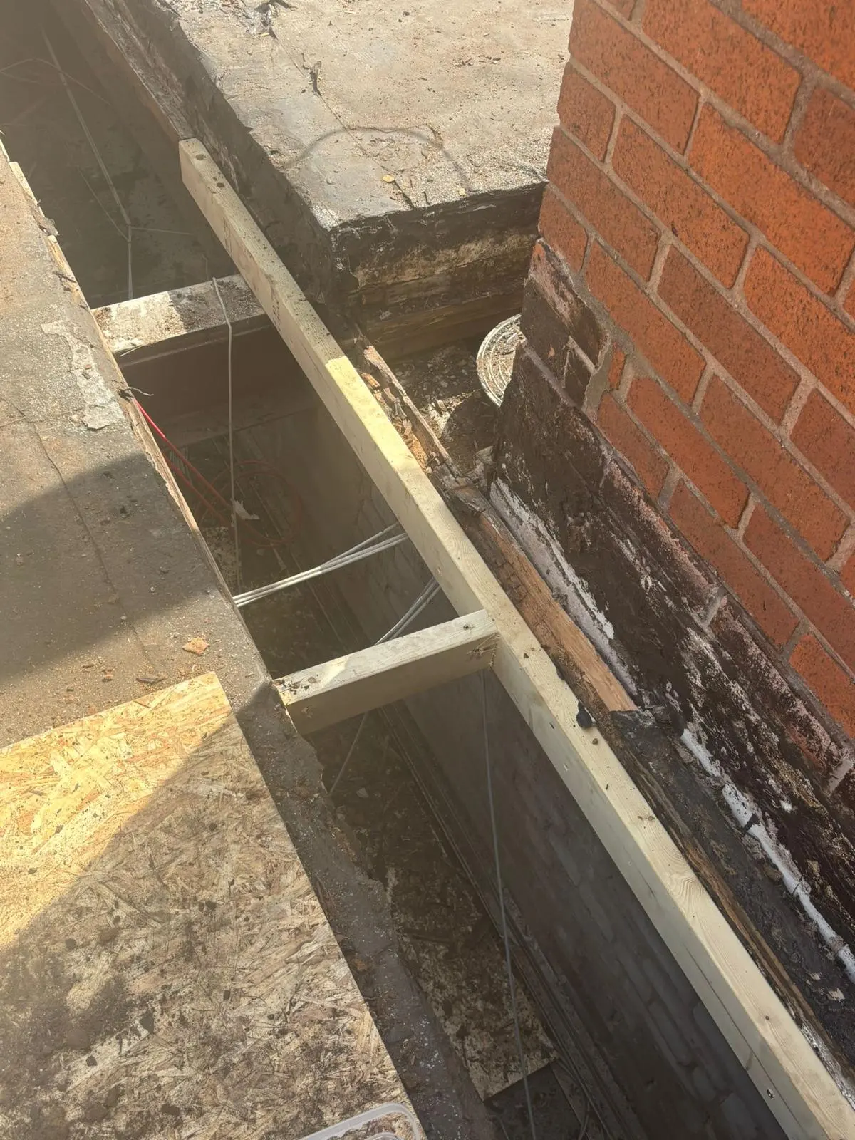 New structural timber joists and OSB decking being installed during flat roof repair work next to a brick wall