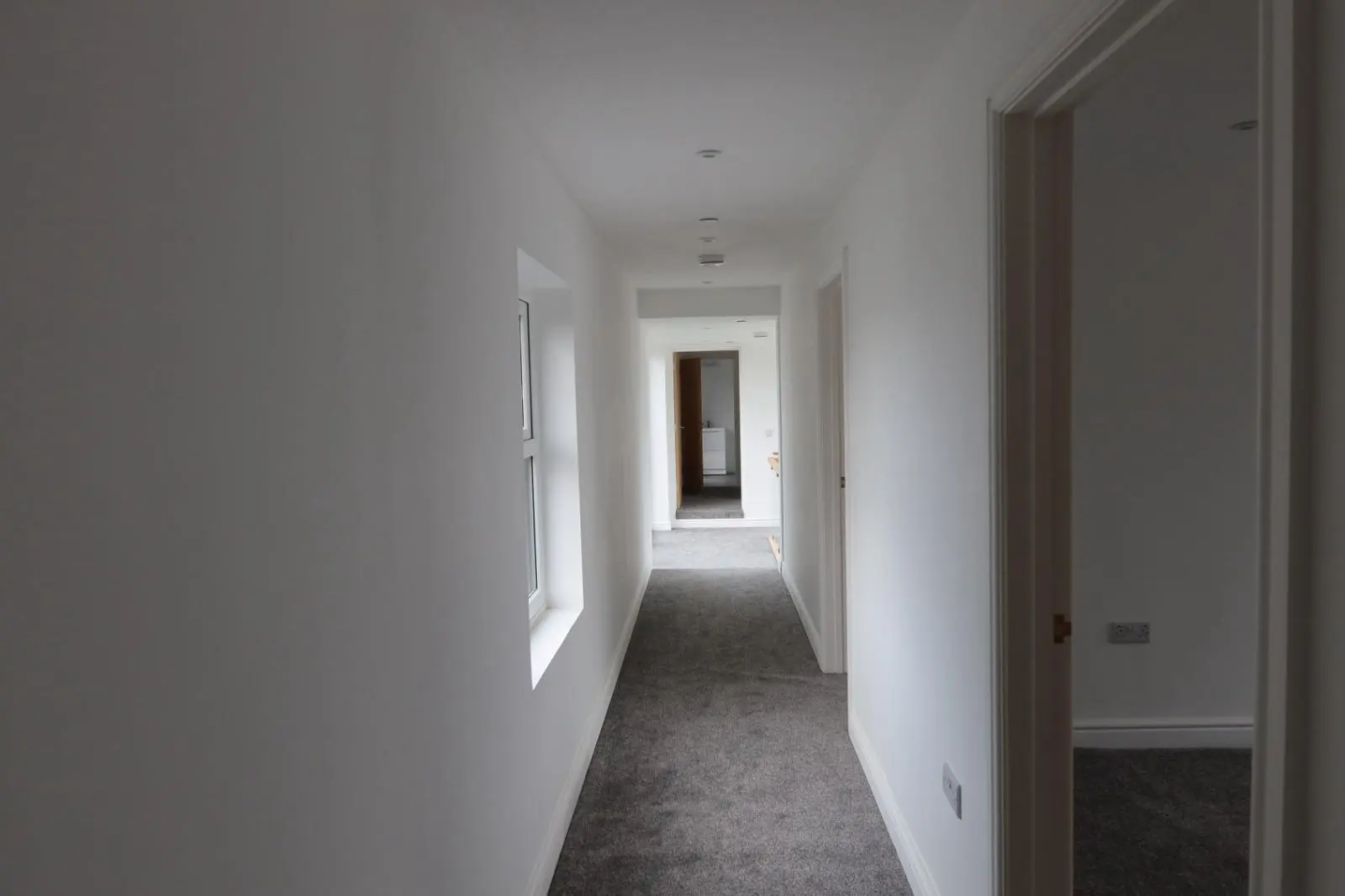 A long, newly renovated residential hallway with fresh white walls and grey carpet, showcasing the clean interior finish provided by Global Energy Insulation and Global Plastering