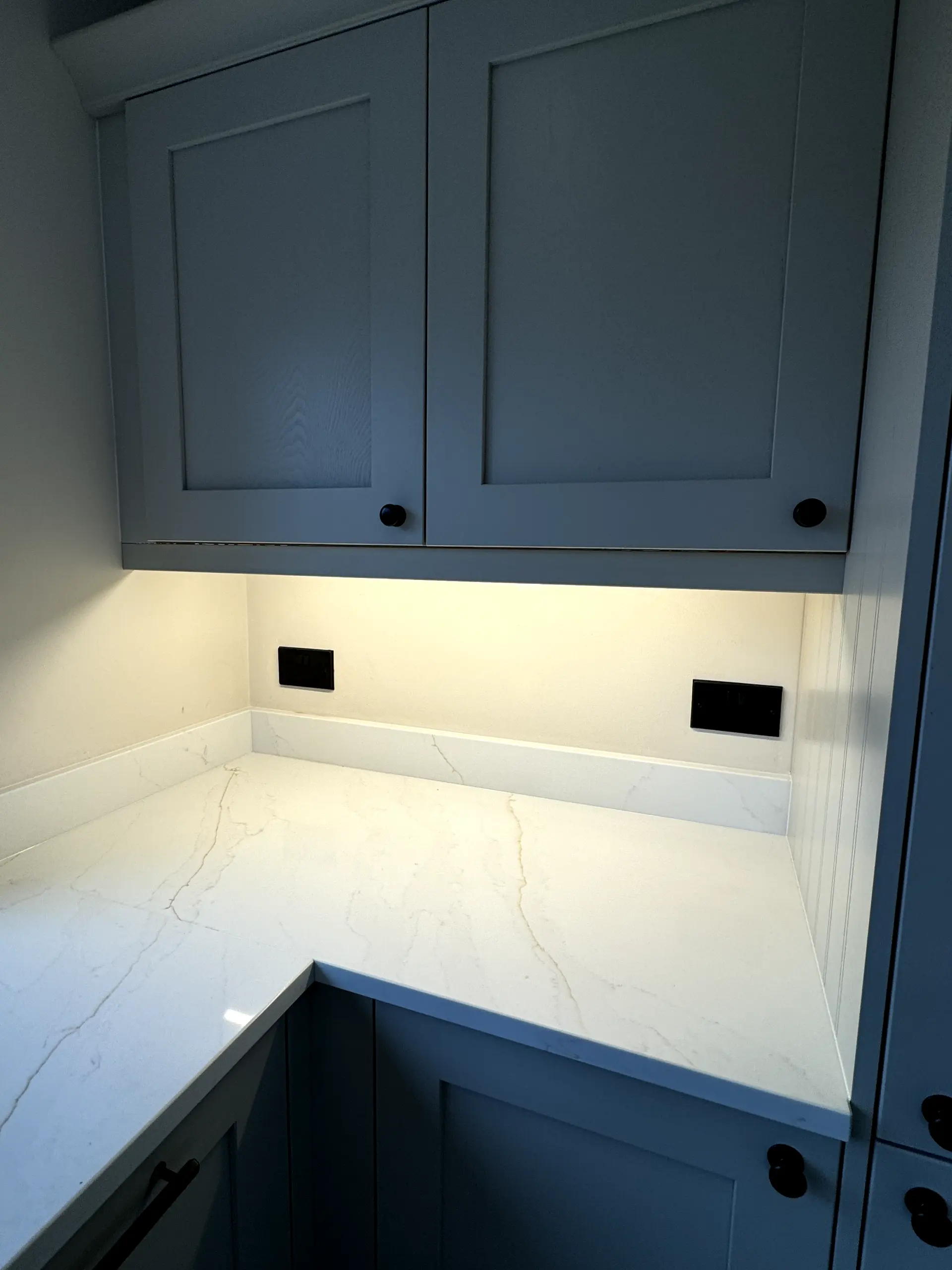 Under-cabinet kitchen lighting and modern black electrical sockets installed above a white worktop