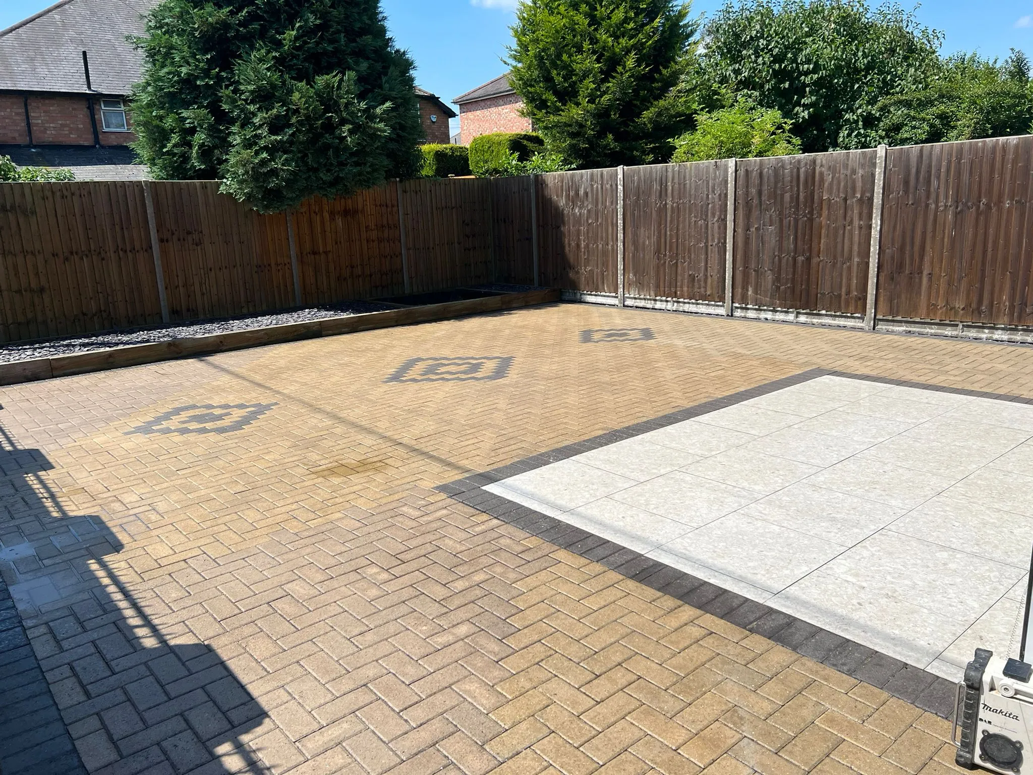 Newly installed garden patio with light brown block paving, a contrasting modern grey slab patio, and a timber fence with a raised gravel bed.