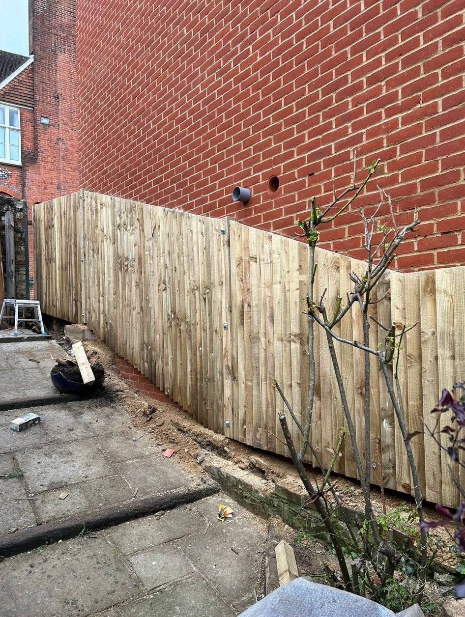 Stepped timber garden fencing installed on a slope next to a brick building.