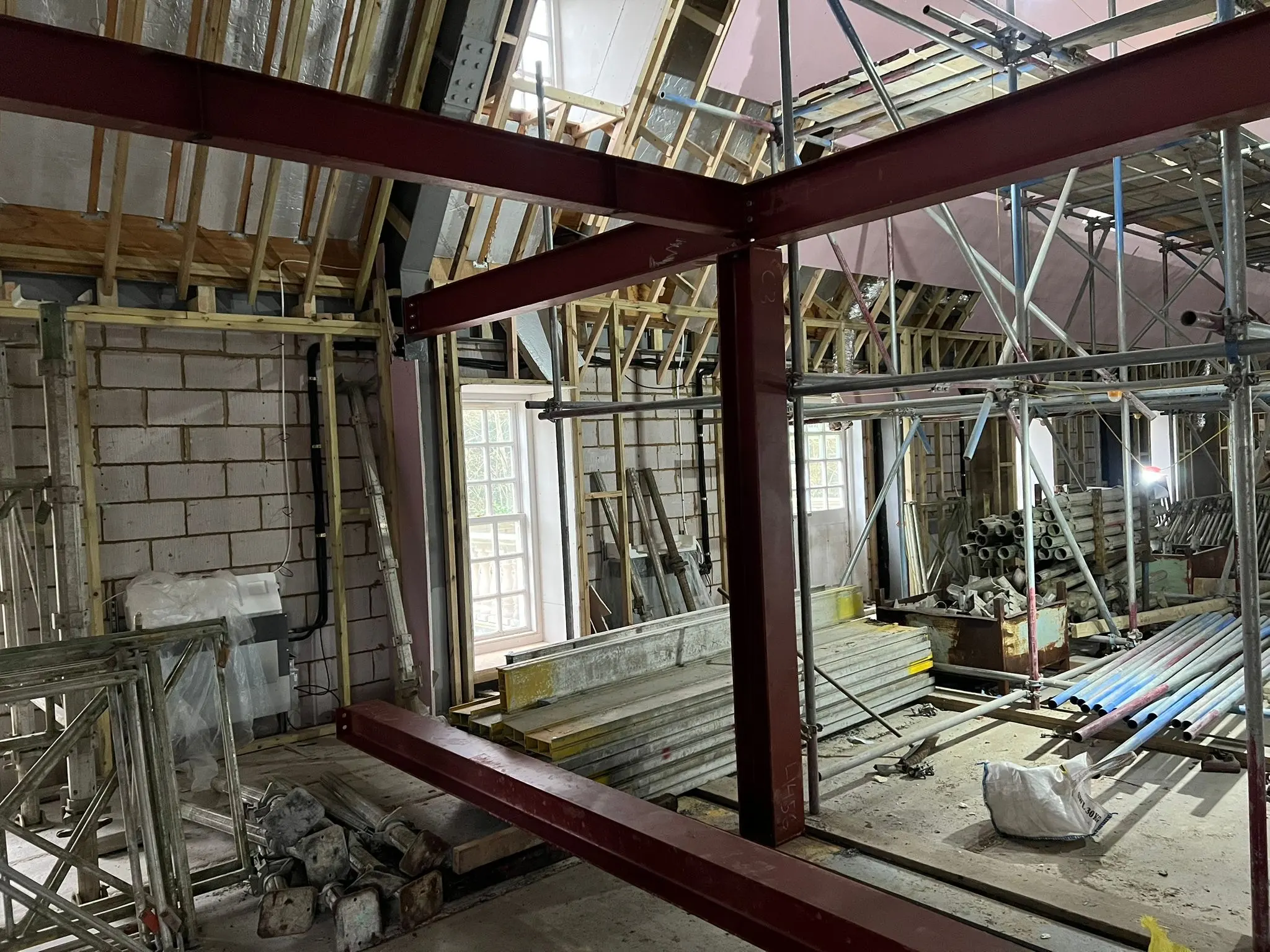 Interior of a building under construction featuring heavy-duty red steel frame erection, blockwork walls, and extensive scaffolding.