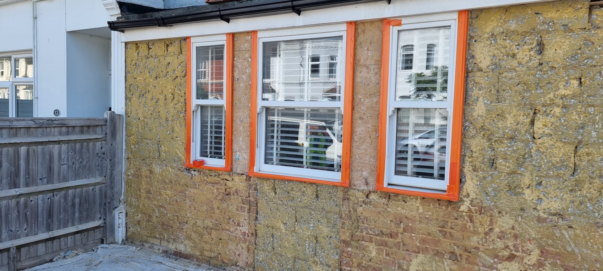 A house wall prepared for external rendering with windows masked for protection.