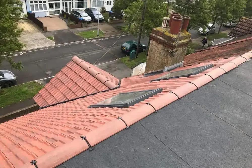 Residential roof with red tiles, flat roof, skylights, and a chimney, viewed from above.